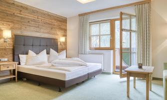 A cozy bedroom with a large bed and wooden walls. There is a balcony with a window and natural light.