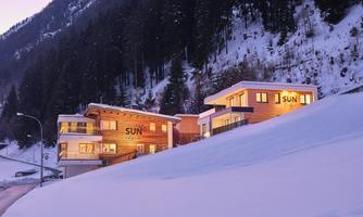 A modern mountain lodge in the snow with warm light. Surrounded by snowy mountains, the scene conveys a cozy atmosphere.