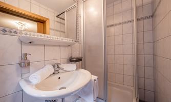 A modern bathroom with a sink, a mirror, and a shower. The walls are tiled in light colors, and the furnishings are clean and functional.