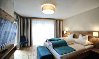 A modern hotel room with a double bed and blue accents. Large windows let in a lot of light and create an inviting atmosphere.