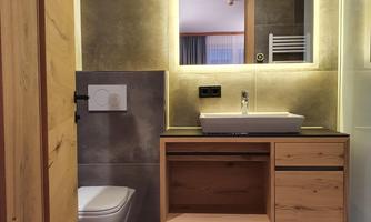 A modern bathroom with wooden details and a large mirror. The walls are clad in gray tiles, and there is a practical sink area.