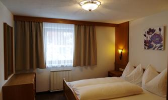 A cozy bedroom with a double bed and light curtains. The walls are painted in warm colors and there is a window with a view outside.
