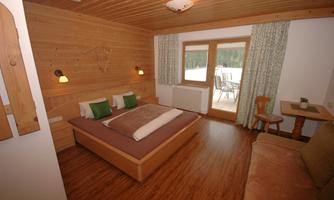 A cozy room with wooden paneling and a double bed. Large windows offer a view of a balcony.