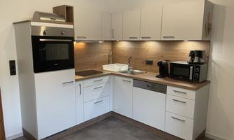 Modern kitchen with white cabinets and wooden surfaces. It is equipped with an oven, a microwave, and a coffee machine.