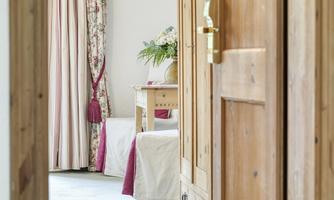 A bright room with wood decor and cozy furniture.  
Curtains with floral patterns and a plant on a table create an inviting atmosphere.