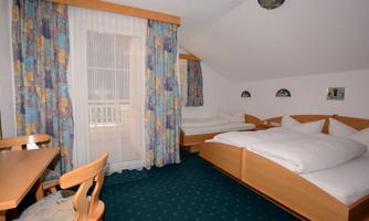 A cozy room with two beds, a table, and a light carpet. Windows with curtains provide daylight and a pleasant atmosphere.