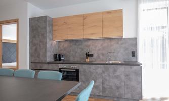 Modern kitchen with gray furniture and wooden elements. A dining table with blue chairs is also visible.