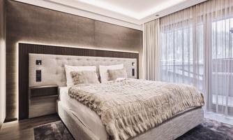A modern bedroom with a large bed and stylish bedding.  
Large windows allow plenty of light in and provide a view outside.