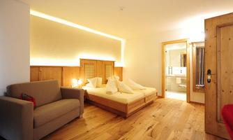 A comfortable room with a bed, a gray sofa, and warm wooden tones. It features soft lighting and access to a bathroom.