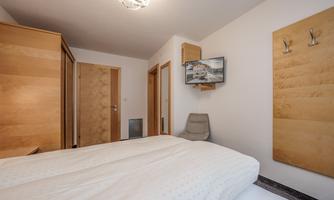 A simple bedroom with a double bed and modern wood paneling. There is a television on the wall and a cozy seating area.