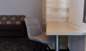 A modern workplace with a table and a comfortable chair. In the background, there is a sofa with a simple pattern.