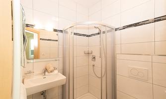 A modern bathroom with a shower, a sink, and a large mirror. The tiles are bright, and the fixtures are simple and elegant.