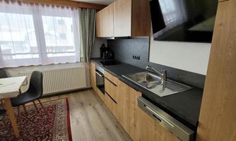 A modern kitchen with wooden cabinets and a large window. The room is bright and well-equipped.