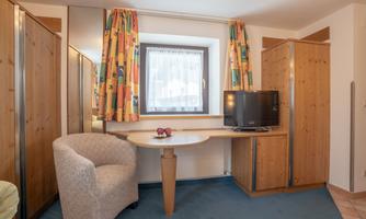 A cozy room with wooden cabinets and a table. A television is on a desk and the window is decorated with colorful curtains.