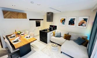 A modern living room with a cozy couch and a dining area. The kitchen is open and well-equipped, with appealing decoration on the walls.