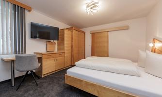 A modern bedroom with a comfortable bed and a flat-screen television. The room is simply and brightly furnished, ideal for relaxing nights.
