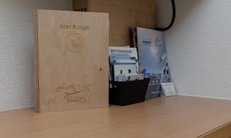 A wooden folder with the inscription "Apart Rüdiger" is on a table. Next to it are informational brochures in a black basket.