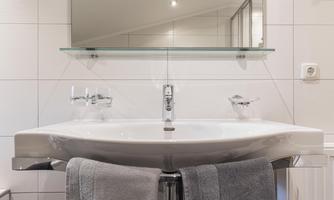 A modern sink with a clear mirror cabinet above it. Towels hang below and the wall is tiled with white tiles.