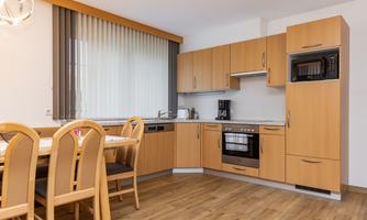 A modern kitchen with wooden furniture and a dining area. The room is bright and friendly with large windows and an elegant design.