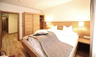A cozy bedroom with a large bed and wooden paneling. The atmosphere is bright and friendly, perfect for relaxing.