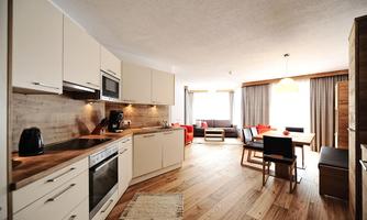 A modern kitchen with wooden shelves and high-quality appliances. The adjoining living area is bright and inviting with comfortable furniture.