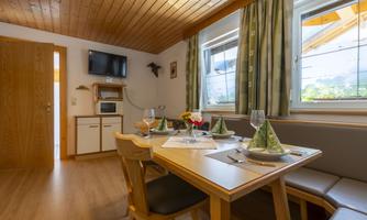 A bright dining room with a large table, filled with dishes and glasses. Large windows let in plenty of light and offer a view outside.