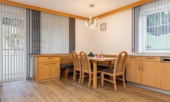 A bright dining room with a wooden table and matching chairs. Large windows with blinds let in plenty of daylight.
