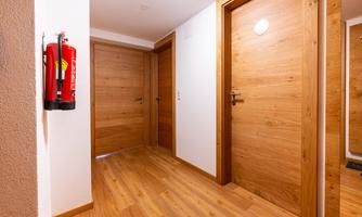 A bright hallway with wooden doors and a modern design. On the wall, there is a fire extinguisher.