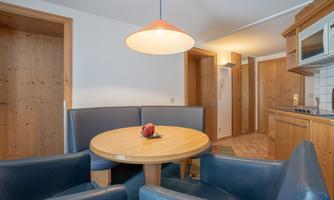 A cozy dining area with a round table and blue chairs. The kitchen is designed in a warm wood tone and offers an inviting atmosphere.