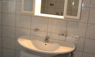 A simple bathroom with a sink and a mirror. The walls are tiled with light tiles.