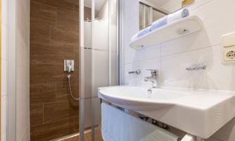 A modern designed bathroom with a shower and a sink. The walls are brightly tiled, with a wooden floor and a small shelf.