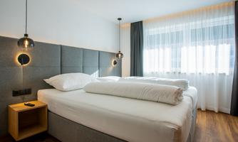 A modern hotel room with two beds and wooden floors. Large windows let in plenty of daylight and give the room a cozy atmosphere.