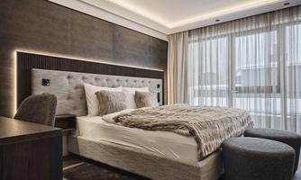 A modern bedroom with a cozy bed and soft lights. Large windows provide plenty of daylight.