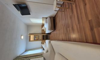 A simple room with two beds, a television, and wooden flooring. The room has large windows and is bright and friendly.