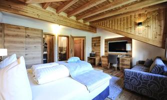 A cozy bedroom with a wooden ceiling and modern furniture. The room has a large bed, a television, and a relaxed seating area.