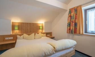A cozy bedroom with a large bed and wood-paneled walls. Colorful curtains and soft lighting create a relaxing atmosphere.