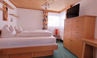 A cozy bedroom with two beds and a wooden ceiling. There is a television and a wooden wardrobe.