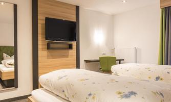 A modern hotel room with two beds, a TV on the wall, and a desk. The walls are light and adorned with subtle decoration.