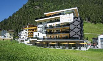 A modern hotel in the Alps with views of green meadows and forests. It features spacious balconies and an inviting terrace.