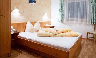 A cozy bedroom with a wooden bed and soft pillows. Gentle light falls into the room through the window.