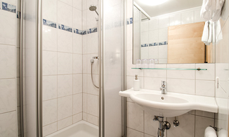 A modern bathroom with a shower and a sink. The walls are tiled in light colors, and there is a mirror above the sink.