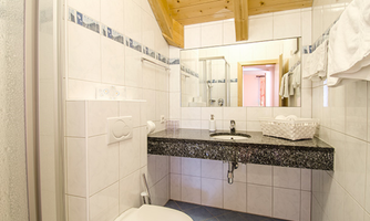 A modern bathroom with tiled walls and a stylish sink. The bright wooden ceiling creates a cozy atmosphere.