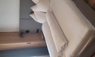 A modern bedroom with a double bed and two extra pillows. The walls are painted in neutral colors and plenty of light streams through the window.