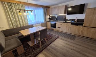 A modern kitchen with a dining table and chairs. The interior is made of wood and has large windows for plenty of daylight.
