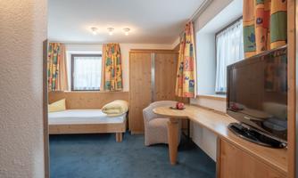 A cozy hotel room with a single bed, a television, and a table. The colorful curtains and the wood interior create an inviting atmosphere.