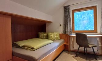 A simple room with a single bed and a desk. The window offers a view of nature.