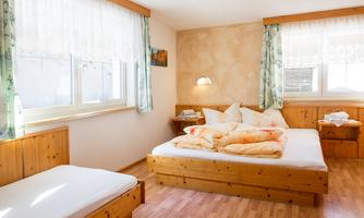A cozy bedroom with a double bed and a single bed. Bright windows create a friendly atmosphere.