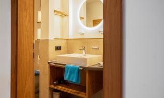 A modern bathroom with a sink and a round mirror. Towels and equipment are neatly stored.