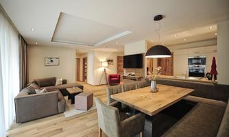 A modern living kitchen with a large dining table and cozy sofas. Plenty of light streams through the windows, creating an inviting atmosphere.