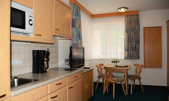 A cozy kitchen with wooden cabinets, a table, and chairs. The room is bright and friendly with a window that lets in light.